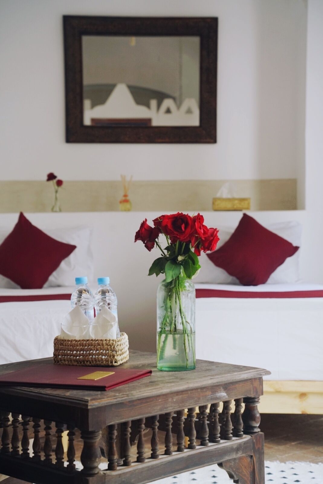 A hotel room with a bed, a bedside table with a vase of red roses, and two water bottles.
