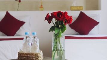 A hotel room with a bed, a bedside table with a vase of red roses, and two water bottles.