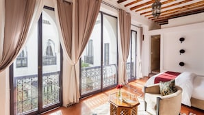 A spacious room with large windows, a balcony, a bed, a chair, and a small table with a vase of flowers. - Riad Twilight (Marrakech)