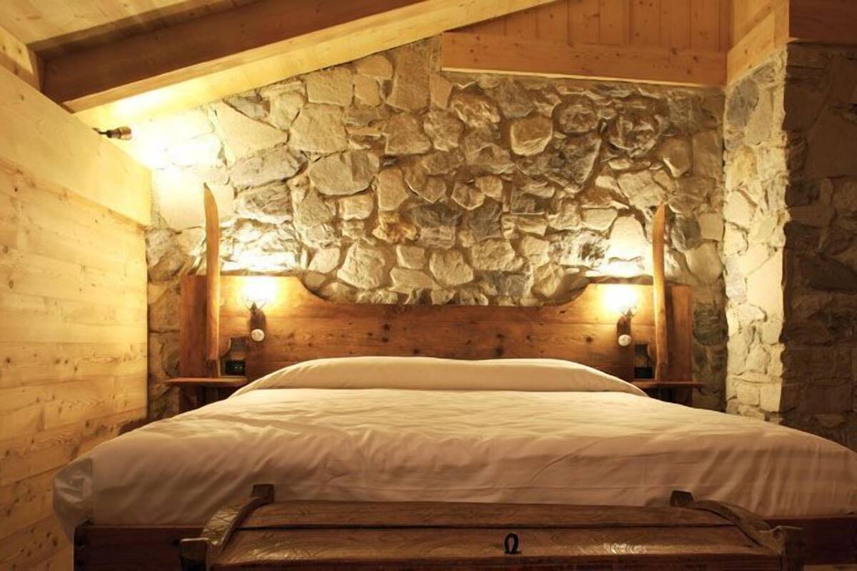A bedroom with a stone wall, wooden beams, and a bed with white bedding.