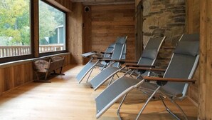 Una habitación con paredes de madera y una pared de piedra, que incluye varias sillas reclinables y un banco de madera.