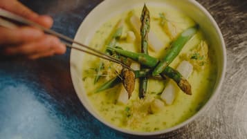 A bowl of food with green vegetables and herbs, placed on a wooden surface.