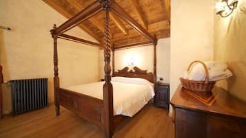 A four-poster bed with a wooden headboard, a nightstand, a wall-mounted lamp, and a wicker basket with towels.