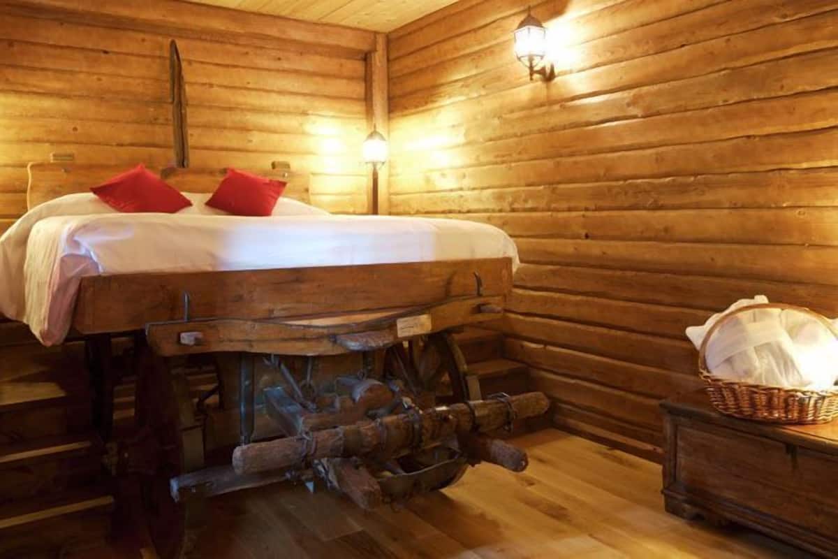 A wooden cabin room with a bed, two wall-mounted lamps, and a rustic wooden table with a basket.