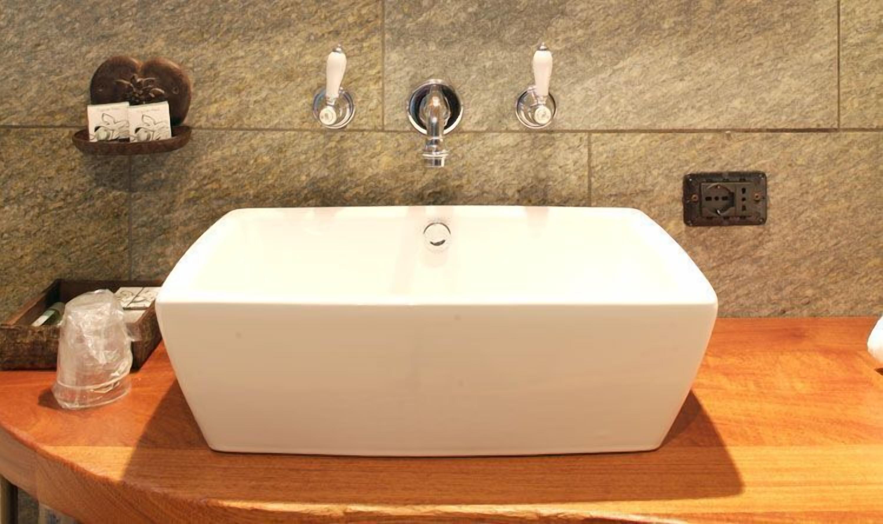 A rectangular white bathroom sink with two faucets on either side, set against a tiled wall.