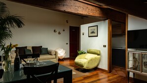 En moderne stue med sofa, lænestol i grøn farve, spisebord med stole og fjernsyn på et skab.