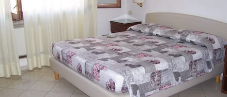 A bedroom with a bed, a bedside table, a mirror, and a window with curtains.