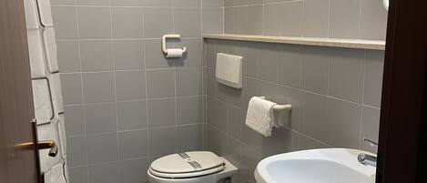 Et badeværelse med toilet, bidet og vask. Der er håndklæder hængende på væggen og en håndtørrer.