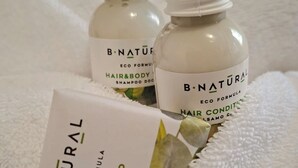 Dos botellas de champú y acondicionador para cabello y cuerpo B-Natural y una pastilla de jabón sobre una toalla blanca.