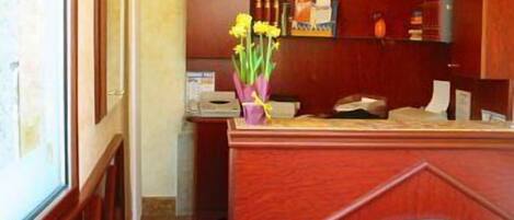 A reception desk with a wooden finish, a nameplate, a vase with yellow flowers, and a shelf with various items.