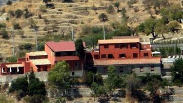 A building with multiple red-roofed structures, surrounded by dry, hilly terrain and sparse vegetation.