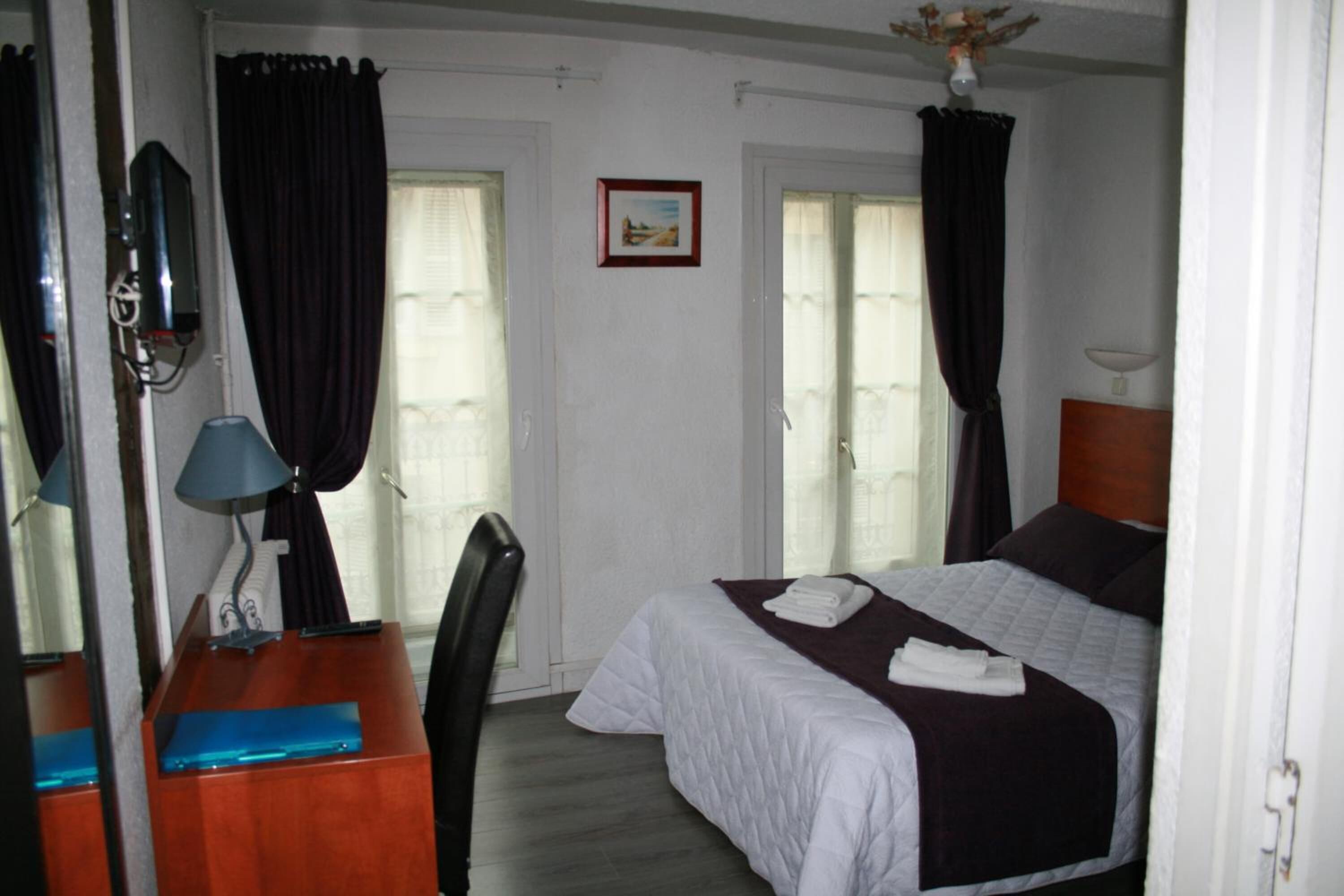 Une chambre d’hôtel avec un lit, un bureau doté d’une lampe, une chaise et une fenêtre avec des rideaux.