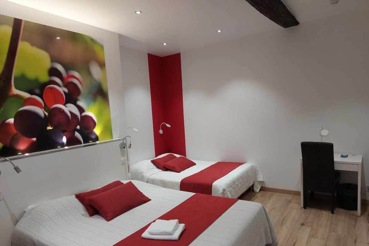 A hotel room with two beds, each with red bedding and pillows, a desk, and a red accent wall.