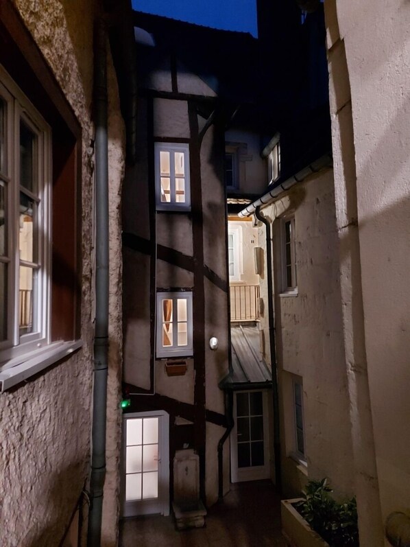 Un estrecho callejón flanqueado por edificios, con varias ventanas y una puerta visible.