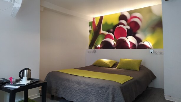 A bedroom with a bed, a nightstand, a green rug, and a wall-mounted picture of fruit. - Le Chambellan (Dijon)