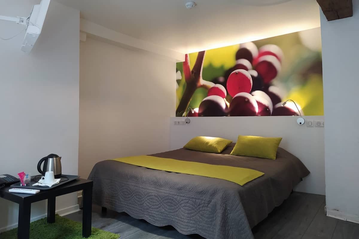 A bedroom with a bed, a nightstand, a green rug, and a wall-mounted picture of fruit.