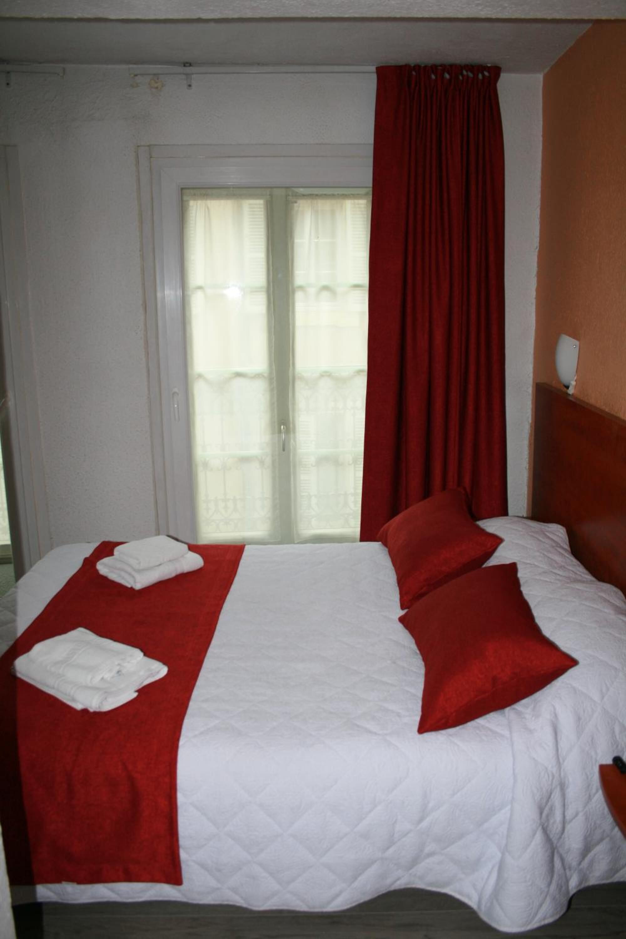 A hotel room with a bed, a window with curtains, and a wall-mounted light fixture.