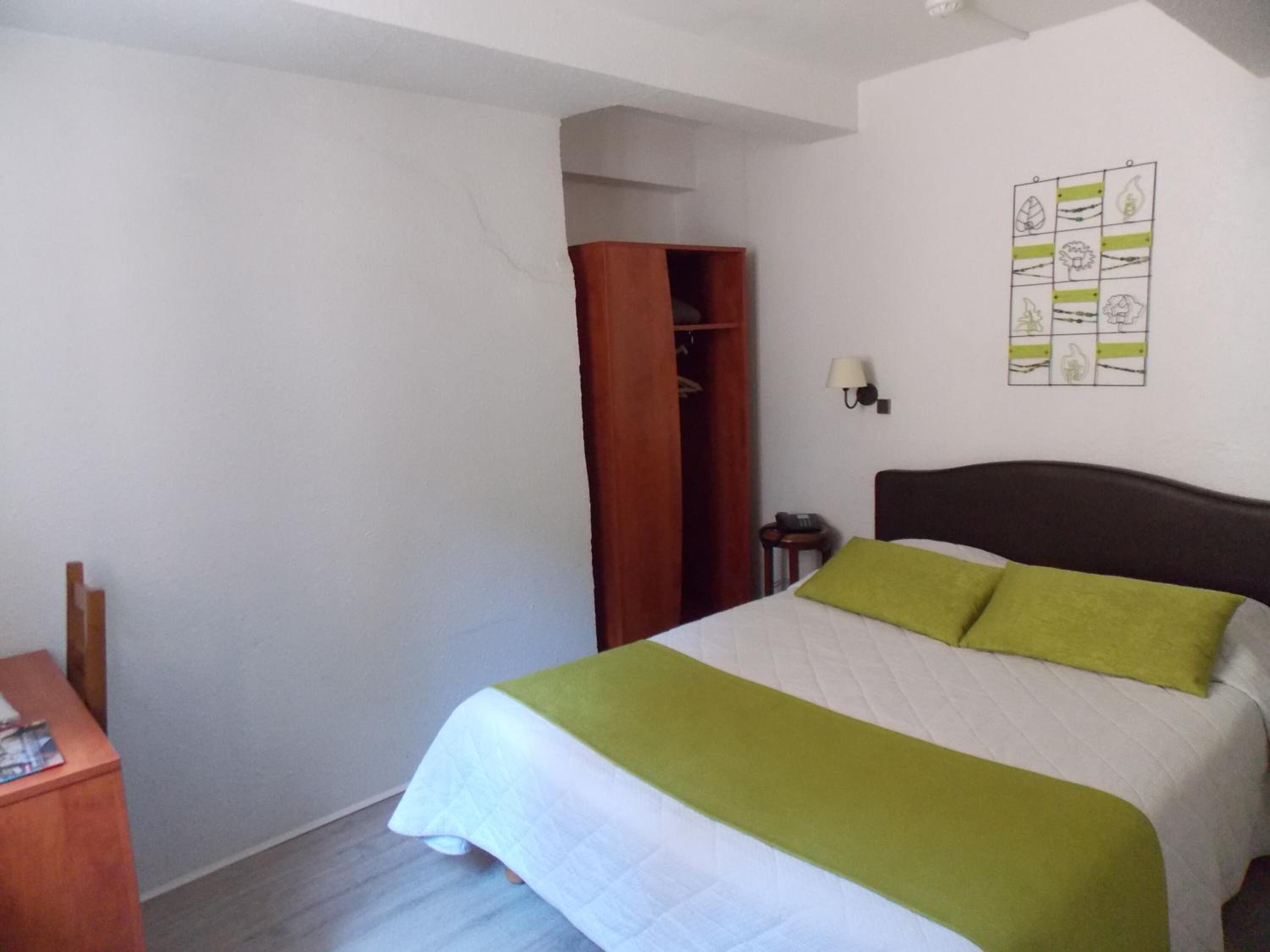 Une chambre à coucher comprenant un lit, une armoire, une table de chevet et une lampe fixée au mur.