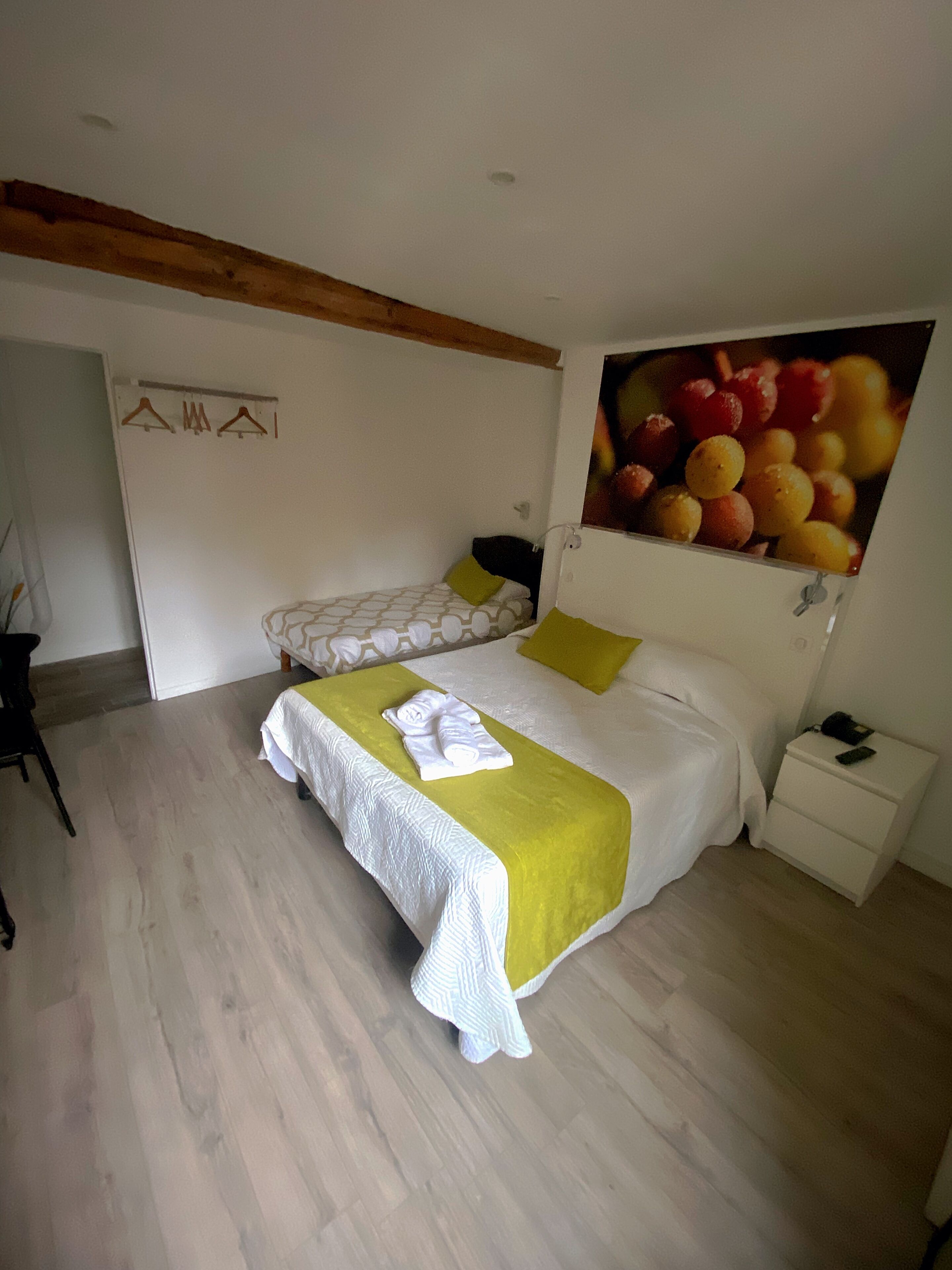 A bedroom with a large bed, a smaller bed, a nightstand, a painting of fruit, and a wooden ceiling beam.