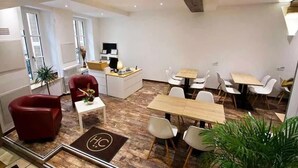 A modern hotel room with a wooden floor, a red chair, a desk with a computer, and a dining area with white chairs. - Le Chambellan (Dijon)