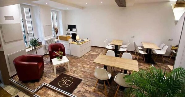 Ein modernes Hotelzimmer mit Holzboden, einem roten Sessel, einem Schreibtisch mit Computer und einer Essecke mit weißen Stühlen.