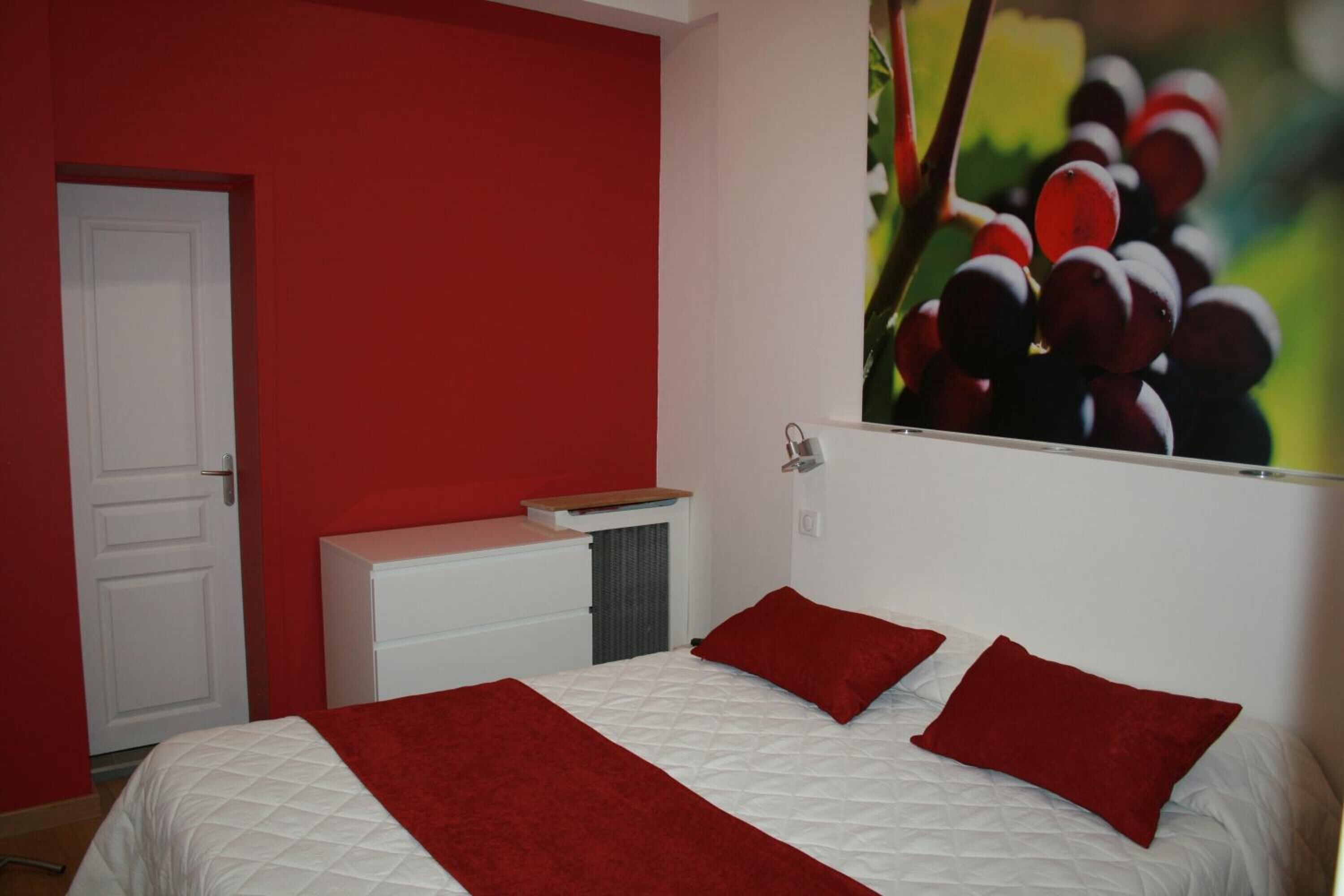 A bedroom with a bed, red pillows, a white dresser, and a red wall.
