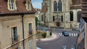 A street view with a prominent church featuring a tall steeple and a clock tower. - Le Chambellan (Dijon)