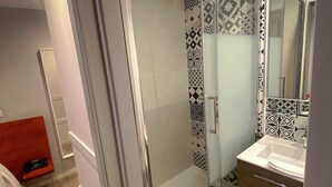 A modern bathroom with a glass shower enclosure, a wooden vanity, and patterned tiles. - Le Chambellan (Dijon)