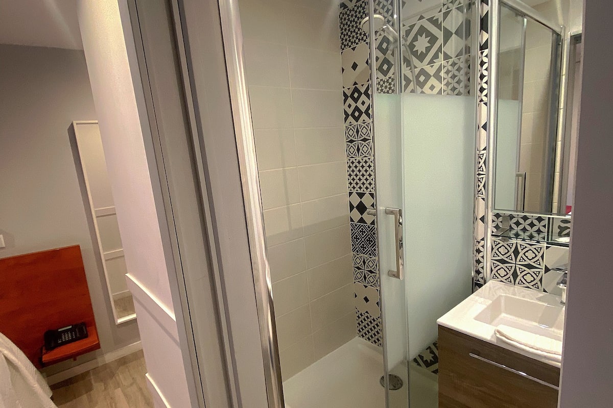 A modern bathroom with a glass shower enclosure, a wooden vanity, and patterned tiles.