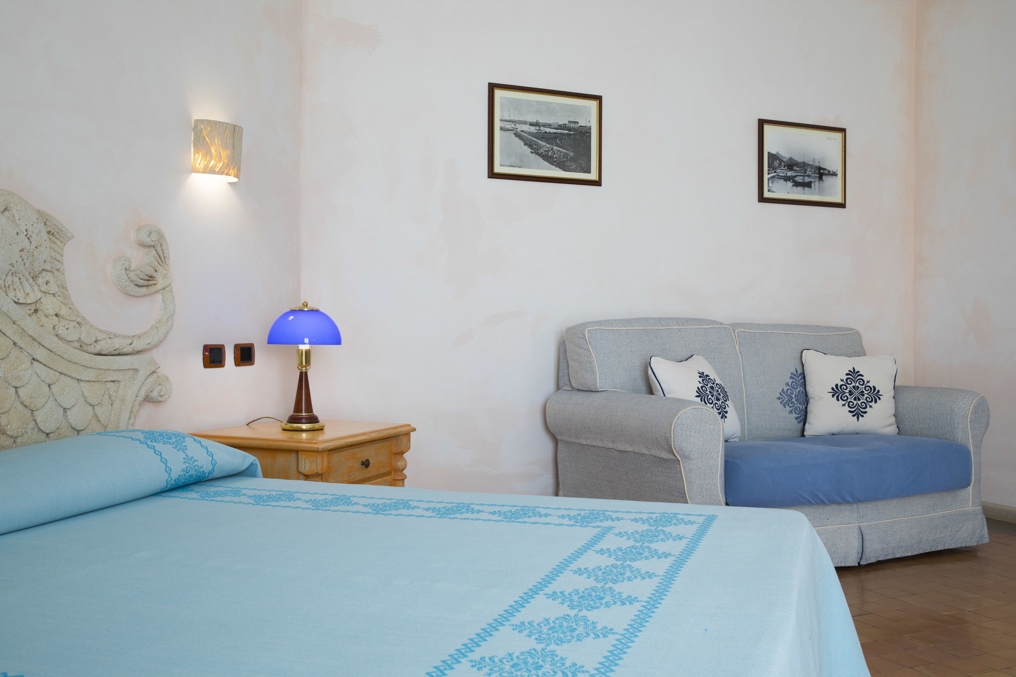 Ein Schlafzimmer mit einem Bett, einem Nachttisch, einer Lampe, einem Schlafsofa und zwei gerahmten Bildern an der Wand.