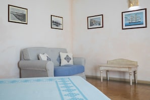 Una habitación con una cama, un sofá gris con cojines azules, una mesita y tres cuadros enmarcados en la pared.