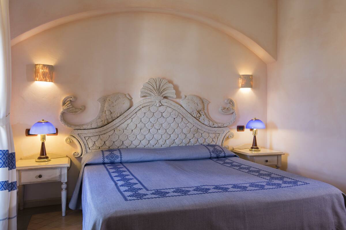 Un dormitorio con una cama grande, dos mesitas de noche con lámparas y un cabecero decorativo.