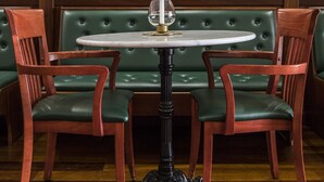 Un banco tapizado de verde con una mesa redonda en el centro, flanqueado por dos sillas de madera.