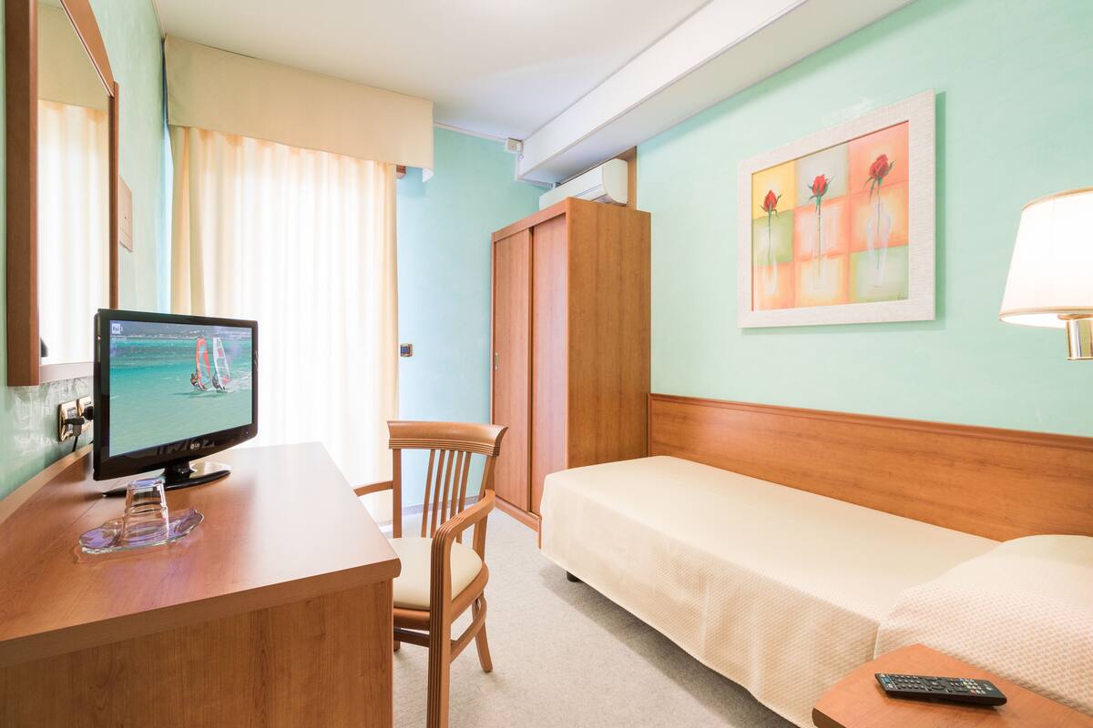 Une chambre d’hôtel comprenant un lit, un bureau avec une télévision, une chaise, une armoire et un tableau au mur.
