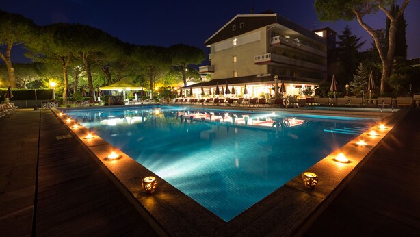 Una piscina nocturna con un edificio al fondo.