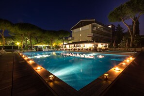 A nighttime swimming pool with a building in the background. - Hotel al Cigno (Lignano Sabbiadoro)