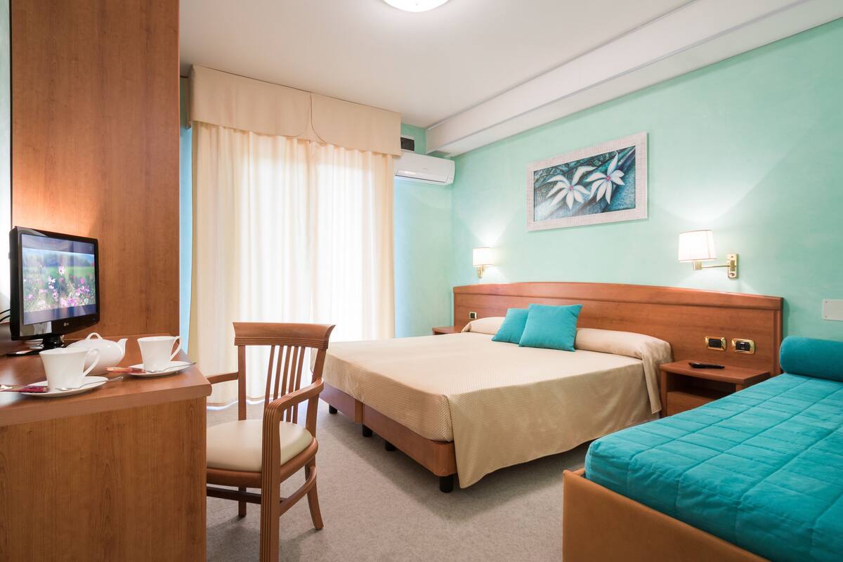 Une chambre d’hôtel avec un lit, un bureau avec une télévision et une chaise.
