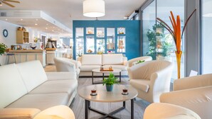 Una sala de estar moderna con una pared azul de acento, sofás blancos, una mesa de centro con una planta y vistas amplias a través de ventanas grandes.
