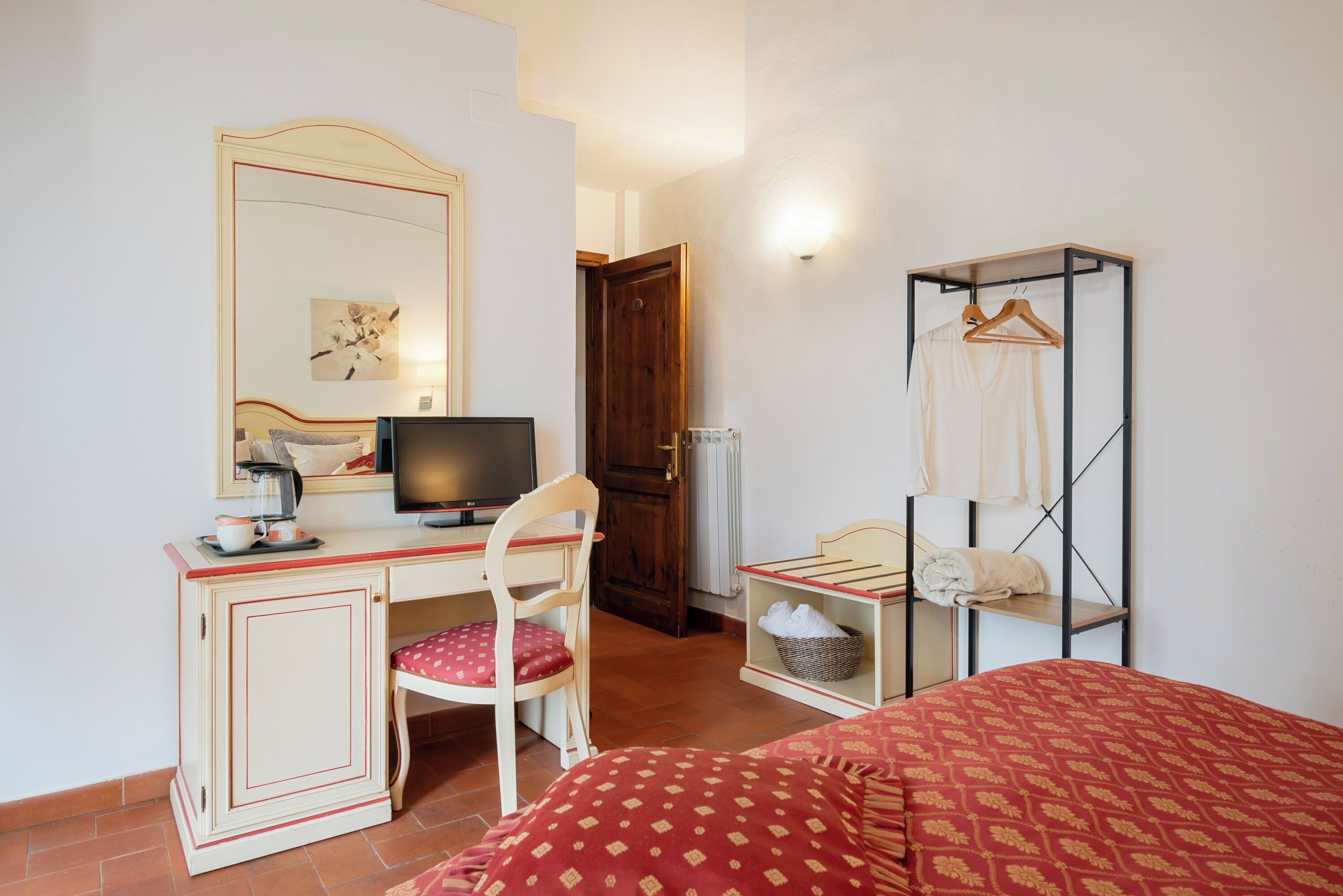 A hotel room with a desk, chair, bed, wardrobe, and a mirror.