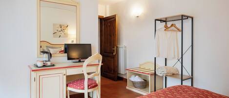 A hotel room with a desk, chair, bed, wardrobe, and a mirror.
