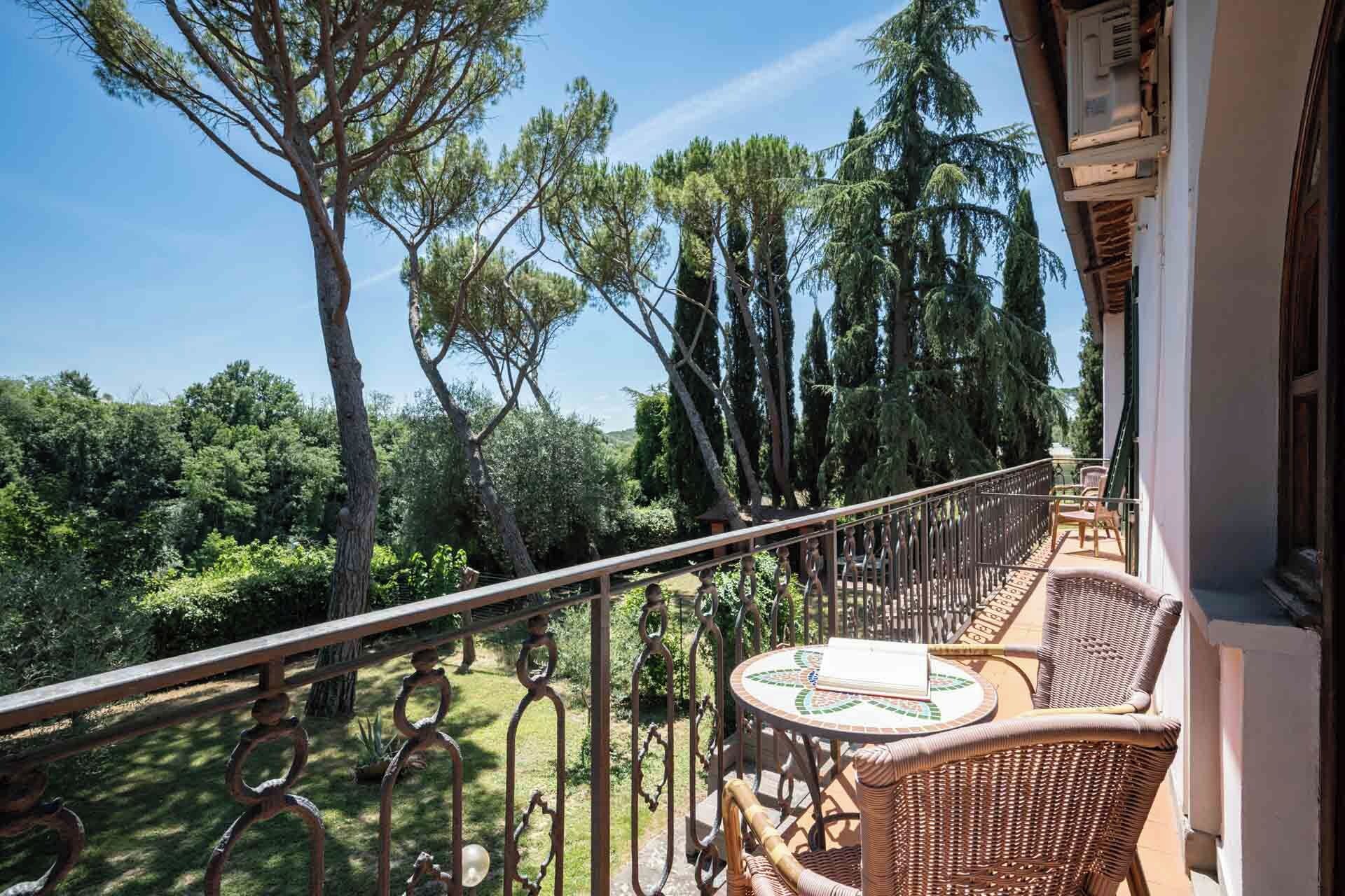Ein Balkon mit Korbmöbeln, einem Metallgeländer und Blick auf Bäume und Grünflächen.