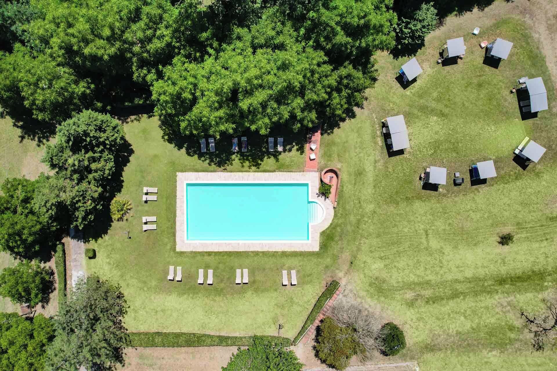 An aerial view of a property with a swimming pool surrounded by lawn chairs and umbrellas, indicating outdoor seating.
