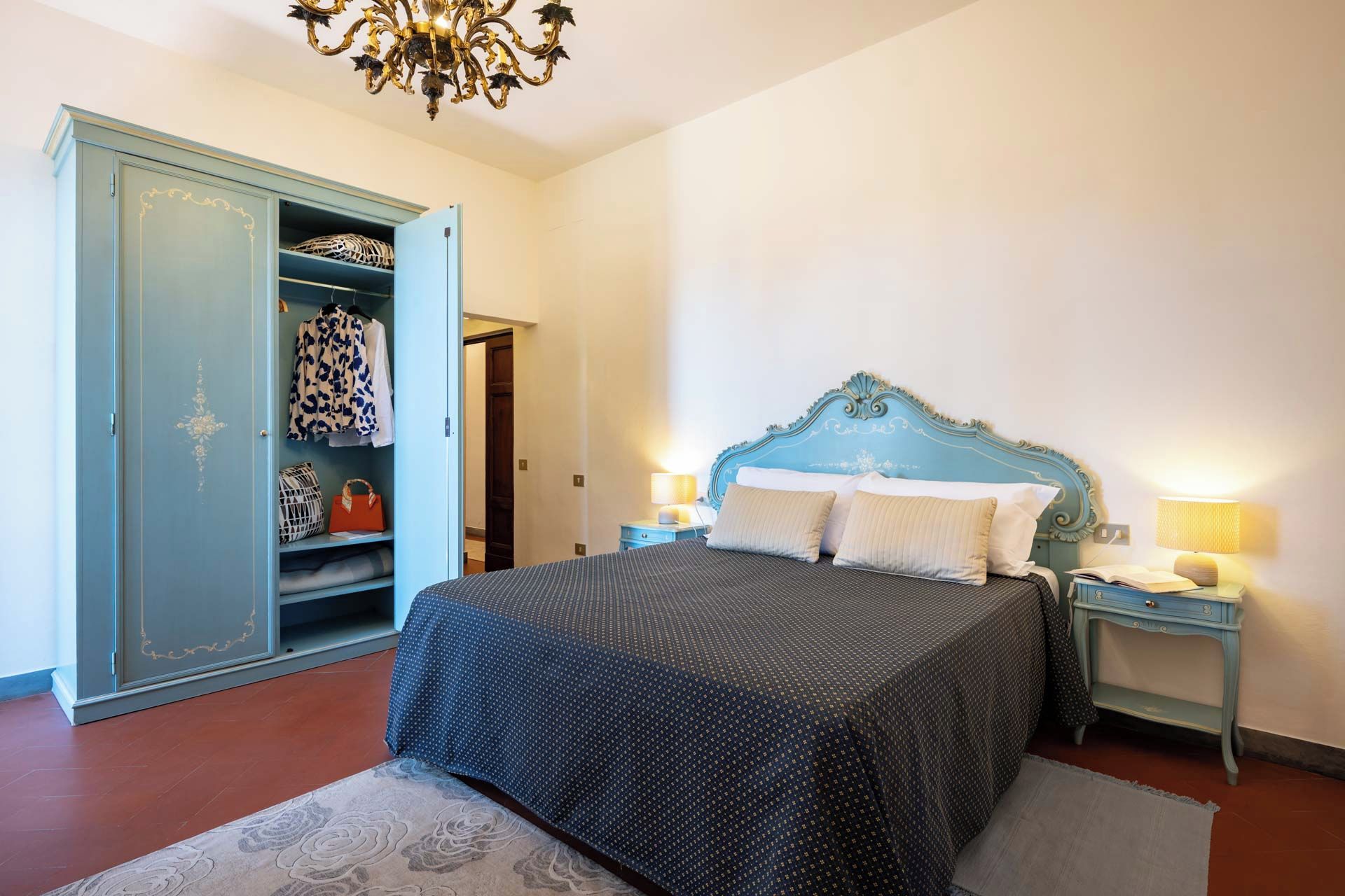 Un dormitorio con cama, mesitas de noche, armario y candelabro.
