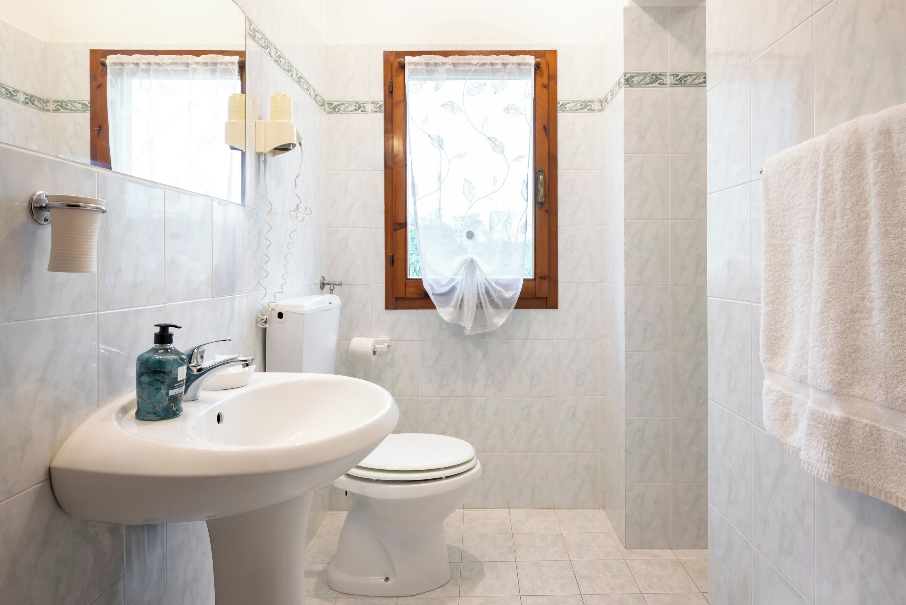 Ein Badezimmer mit Waschbecken, Toilette und einem Fenster mit Vorhängen.