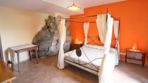 A bedroom with a four-poster bed, a stone wall, and a small table with a lamp. - Casarufolo Paradise (Sorrento)