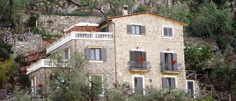 Un edificio de piedra con varios balcones, una escalera y vegetación circundante.