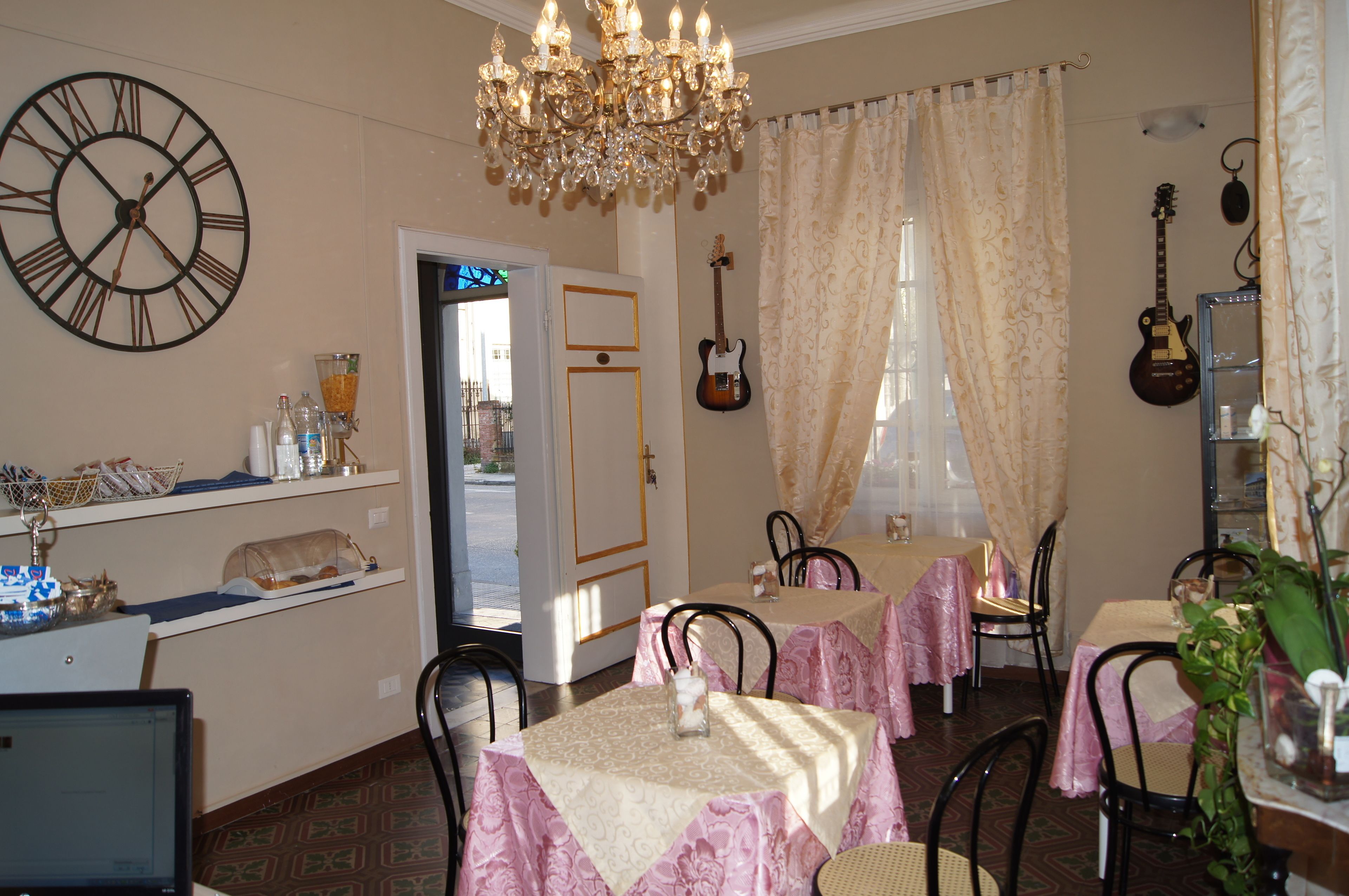 A dining area with tables covered in pink tablecloths, a chandelier, a clock, and a guitar on the wall.