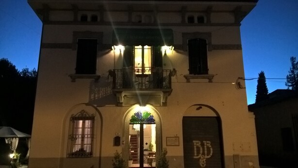 A building with a balcony, a door with a sign, and a window with a curtain. - La Mimosa Bed and Breakfast (Lucca)