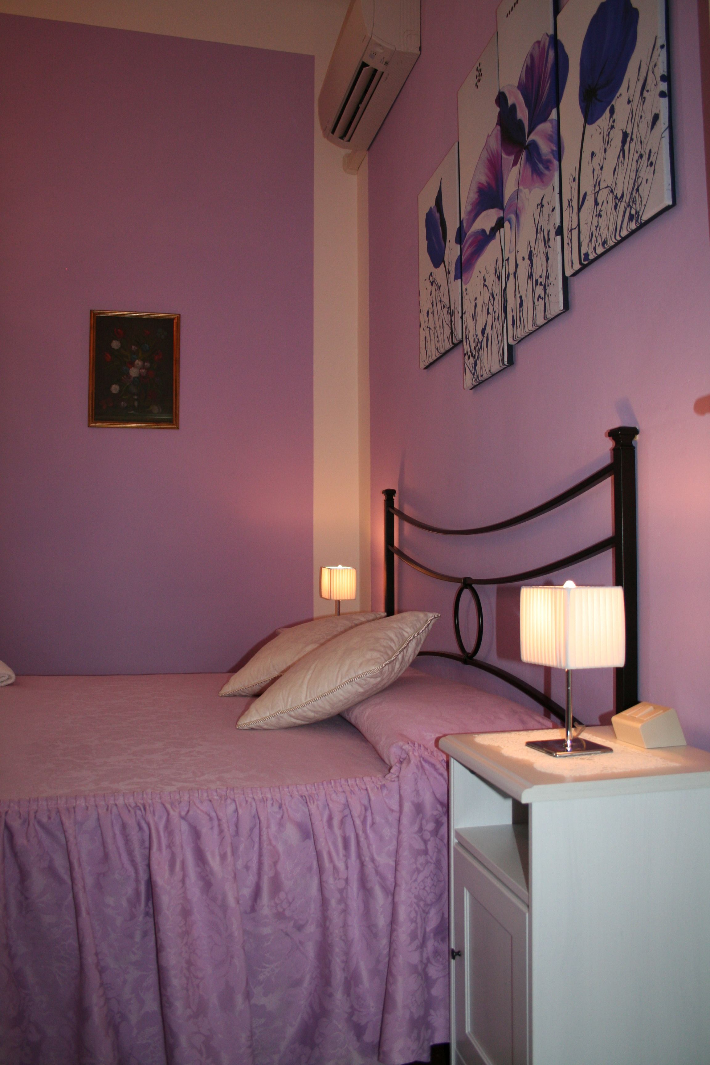 A bedroom with a bed, a nightstand, a lamp, and floral artwork on the wall.