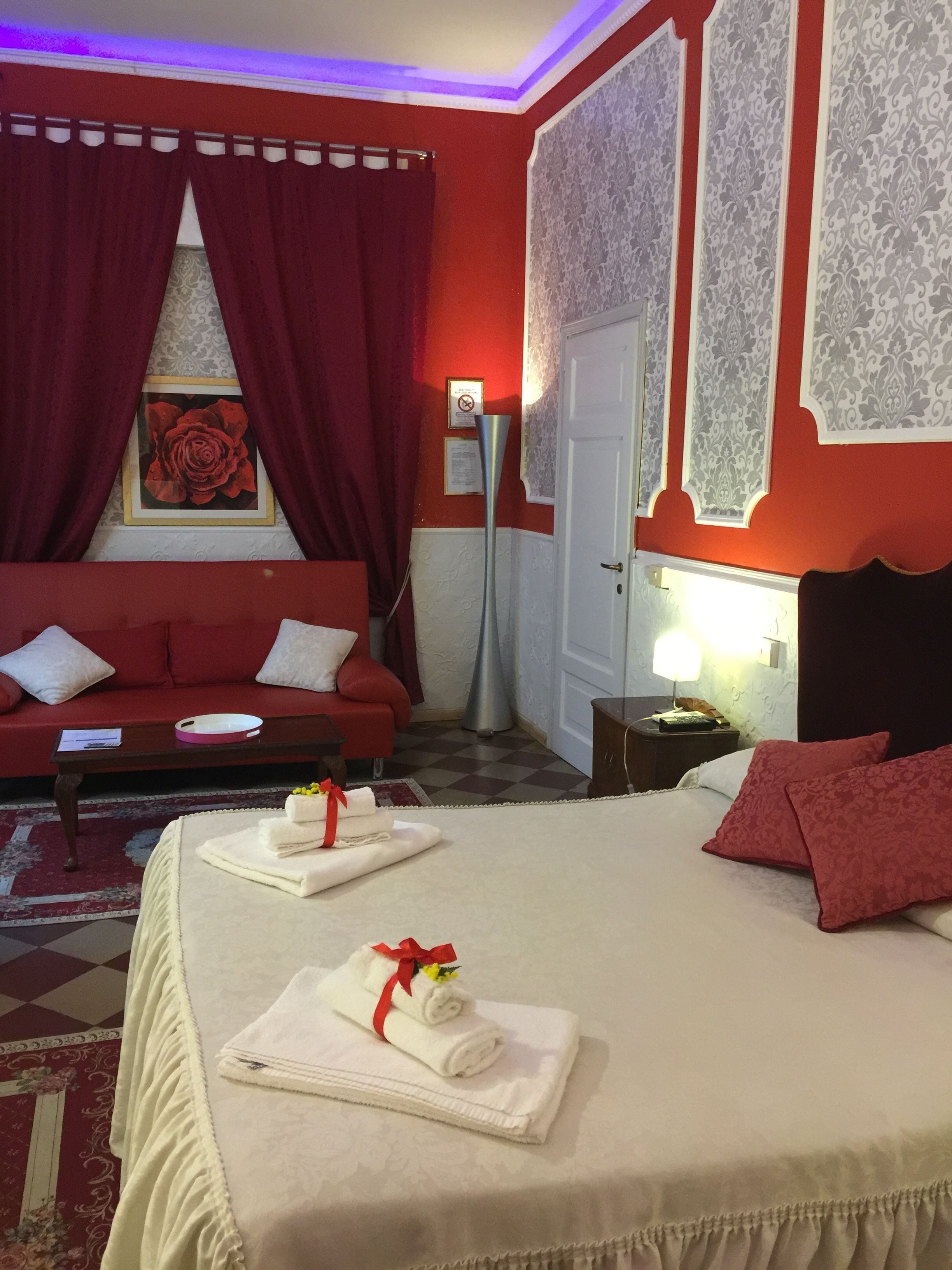 A hotel room with a red sofa, a bed with white linens, and a red curtain.